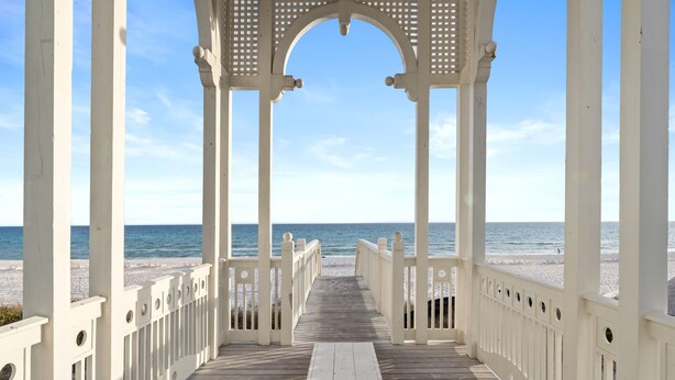 Eine Holzstege führt zu einem Strand mit einem weißen Gazebogebäude.