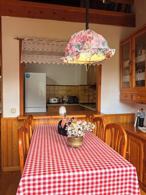 A dining area with a red and white checkered tablecloth, wooden chairs, a floral centerpiece, and a kitchen in the background. - Spacious Duplex with Fireplace, Isard 2 (Pla de l'Ermita)