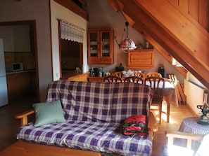 Una sala de estar acogedora con un sofá a cuadros, una mesa de comedor de madera y una zona de cocina con armarios de madera.