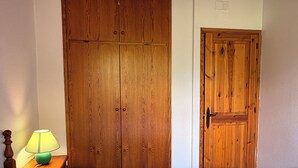 A bedroom with a large bed, a wooden wardrobe, and a smaller door.