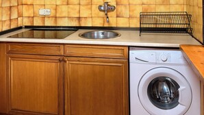 Cozinha compacta com armários de madeira, pia, lava-louças e painel de azulejos.