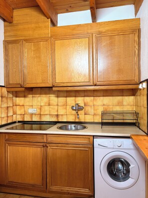 A compact kitchen with wooden cabinets, a sink, a dishwasher, and a tiled backsplash.