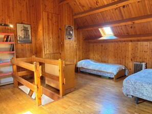 A wooden cabin with two beds, a wooden bench, a radiator, and a skylight.