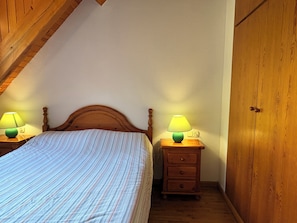 Une chambre à coucher avec une tête de lit en bois, un lit avec une literie à rayures, deux tables de chevet avec des lampes et une armoire en bois.