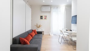 A modern living room with a grey sofa, white curtains, a white table, and a flat-screen TV.