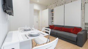 A modern living room with a grey sofa, red cushions, and a white dining table set with plates, glasses, and cutlery.
