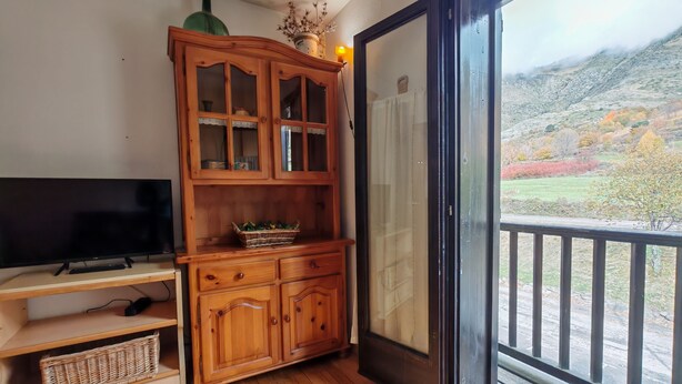 A room with a wooden cabinet, a television, and a view of a mountainous landscape through a glass door. - North facing apartment - Falcó 12 (Pla de l'Ermita)