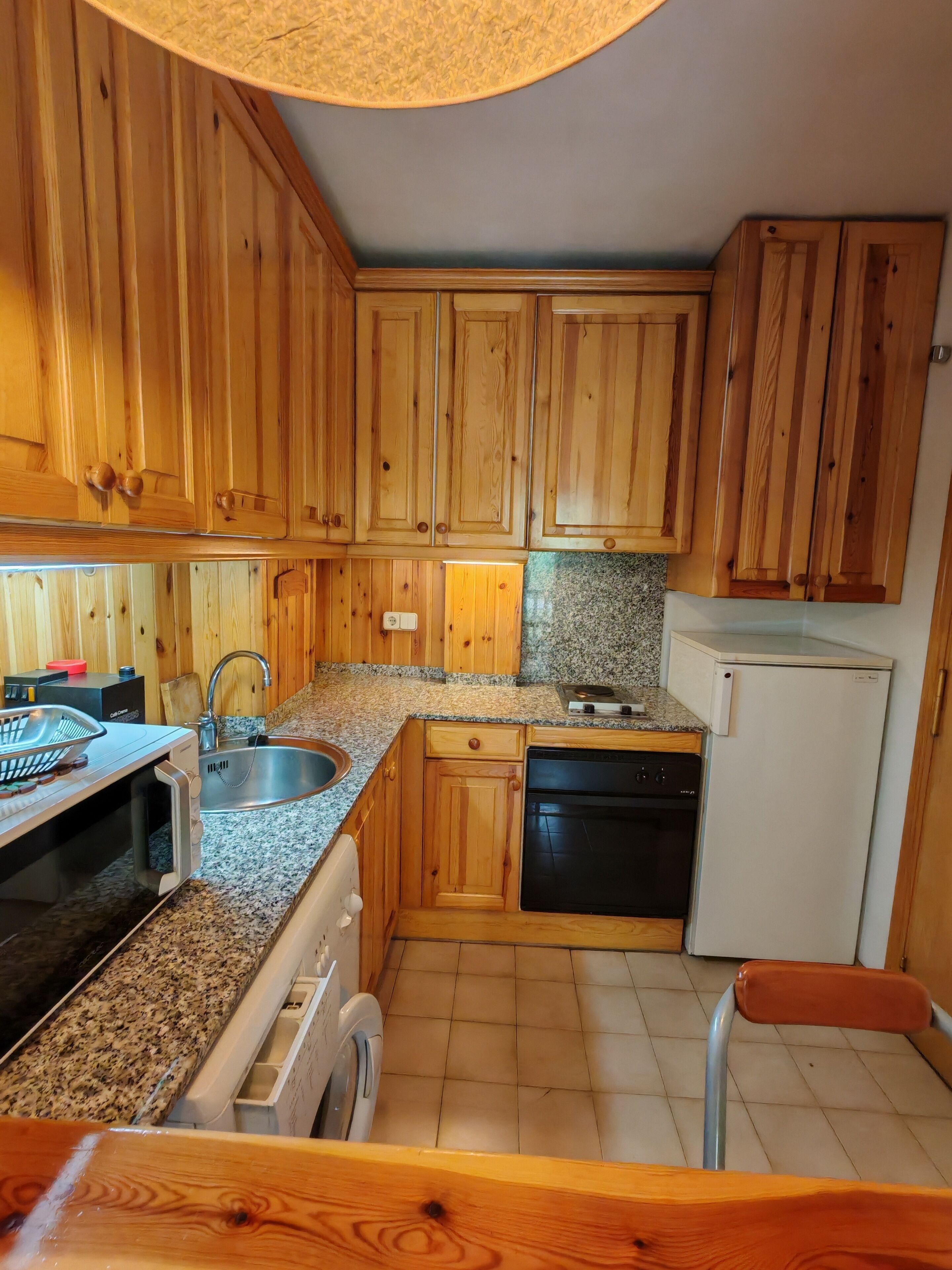 Una cocina con armarios de madera, encimera de granito, fregadero, lavavajillas y microondas.