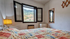 A bedroom with a bed, a nightstand, a lamp, a dresser, and a window with a view of a mountainous landscape. - North facing apartment - Falcó 12 (Pla de l'Ermita)