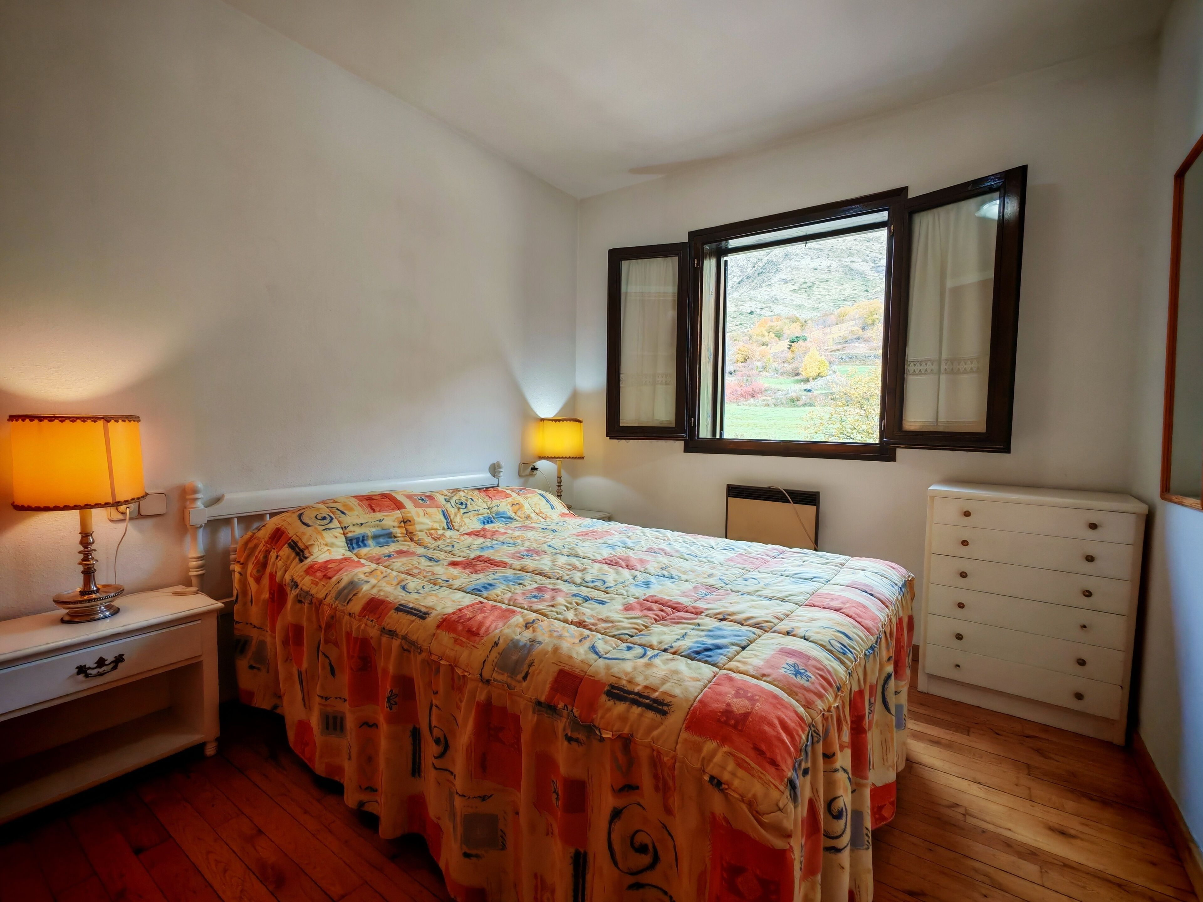 Un dormitorio con cama, lámparas de noche, cómoda y ventana con cortinas.