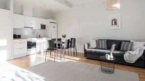 Una cocina moderna con armarios blancos, un comedor con mesa y sillas, y un sofá gris oscuro en una sala de estar.