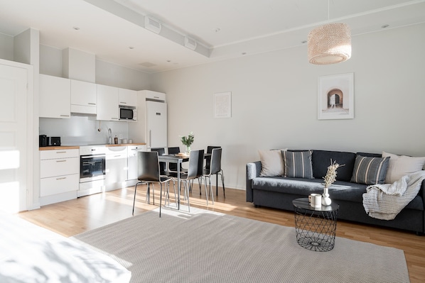 A modern kitchen with white cabinets, a dining area with a table and chairs, and a dark grey sofa in a living room.