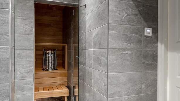 Un baño moderno con baldosas grises, un banco de madera y una sauna integrada.