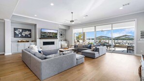 A spacious living area with a large sofa set, a flat-screen TV mounted on the wall, and a view of the outdoor patio area.