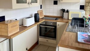 A compact kitchen with a built-in oven, a bread box, a microwave, and a sink with a dish rack. - Stable Cottage, Old Mill Farm, Cotswold Water Park (Cirencester)