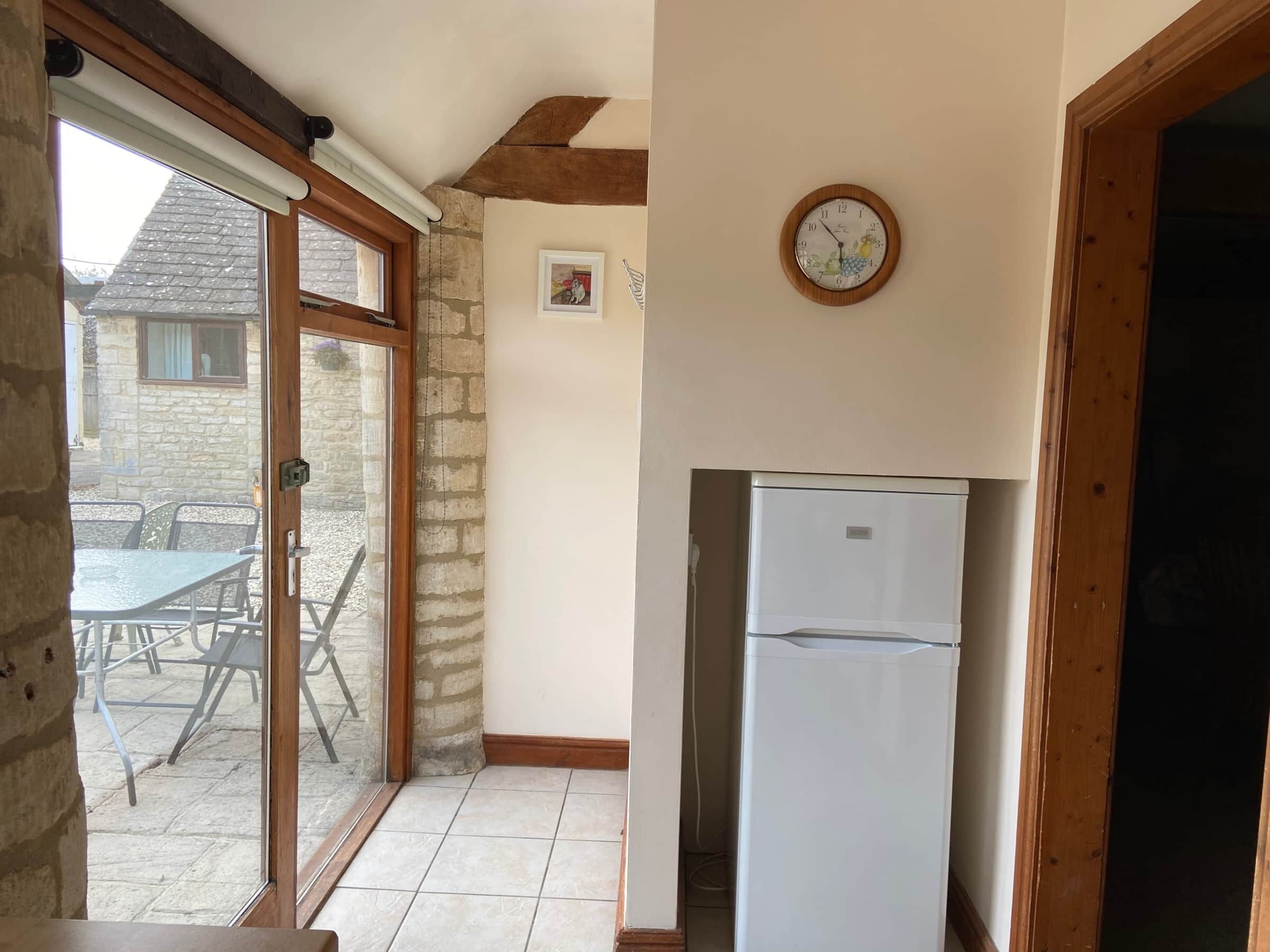 A kitchen with a white refrigerator, a wooden door frame, and a window with a view of a stone building and outdoor furniture.