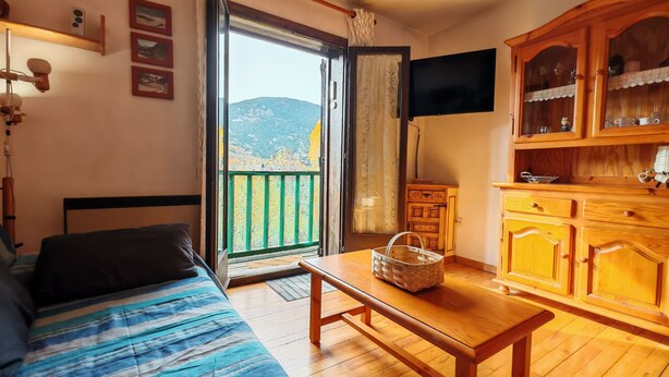 Een kamer met een bed, een houten tafel, een televisie en uitzicht op bergen door een groot raam.