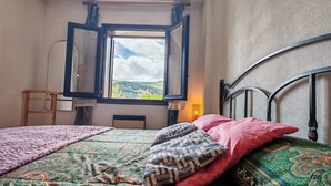 Een slaapkamer met een bed, een raam met gordijnen, een stoel en een lamp.