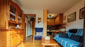Een gezellige woonkamer met een bank, een fauteuil, houten kasten en een keukenhoek.
