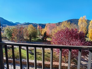 Un balcón con vista a un parque, árboles y montañas.