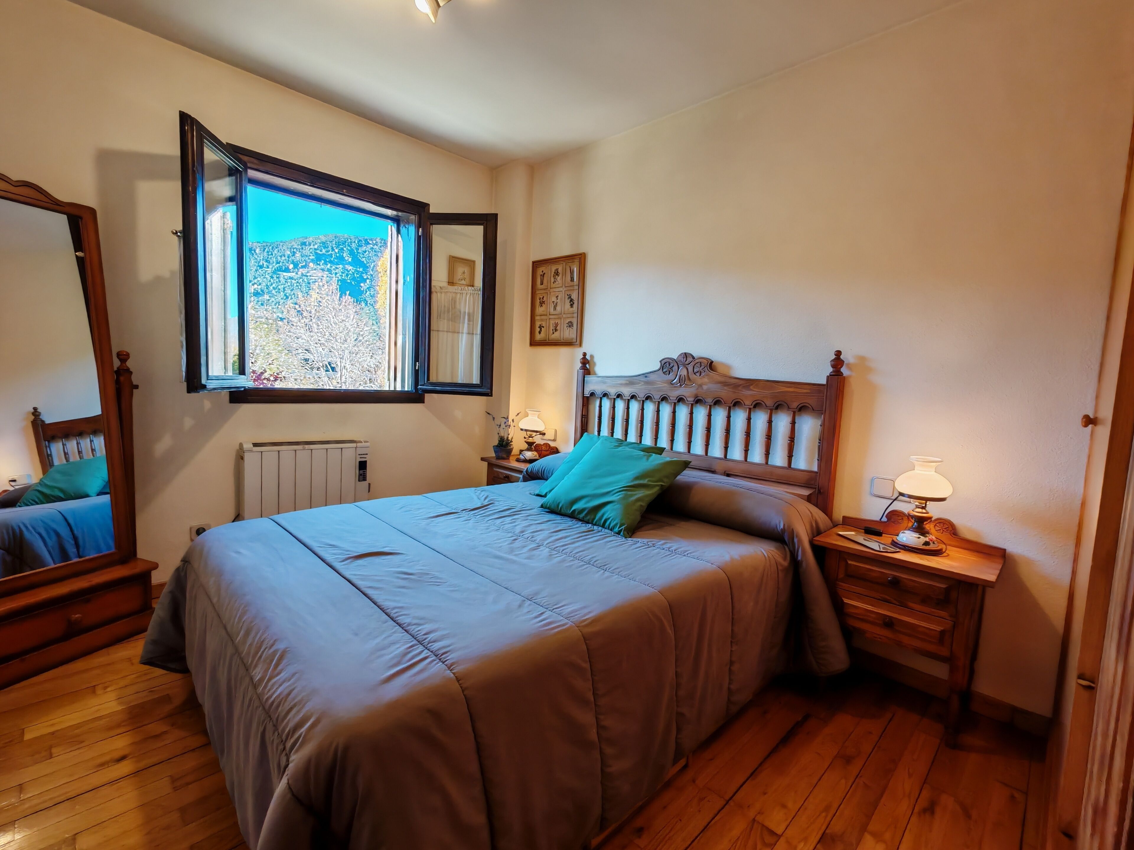 Een slaapkamer met een groot bed, een raam met uitzicht, een nachtkastje met een lamp en een radiator.