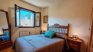 Une chambre avec un grand lit, une fenêtre donnant sur un beau paysage, une table de chevet avec une lampe et un radiateur.