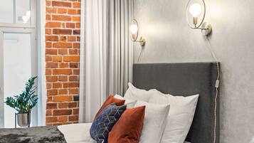 Un dormitorio moderno con pared de ladrillo, cabecera gris y cama con almohadas blancas y estampadas.