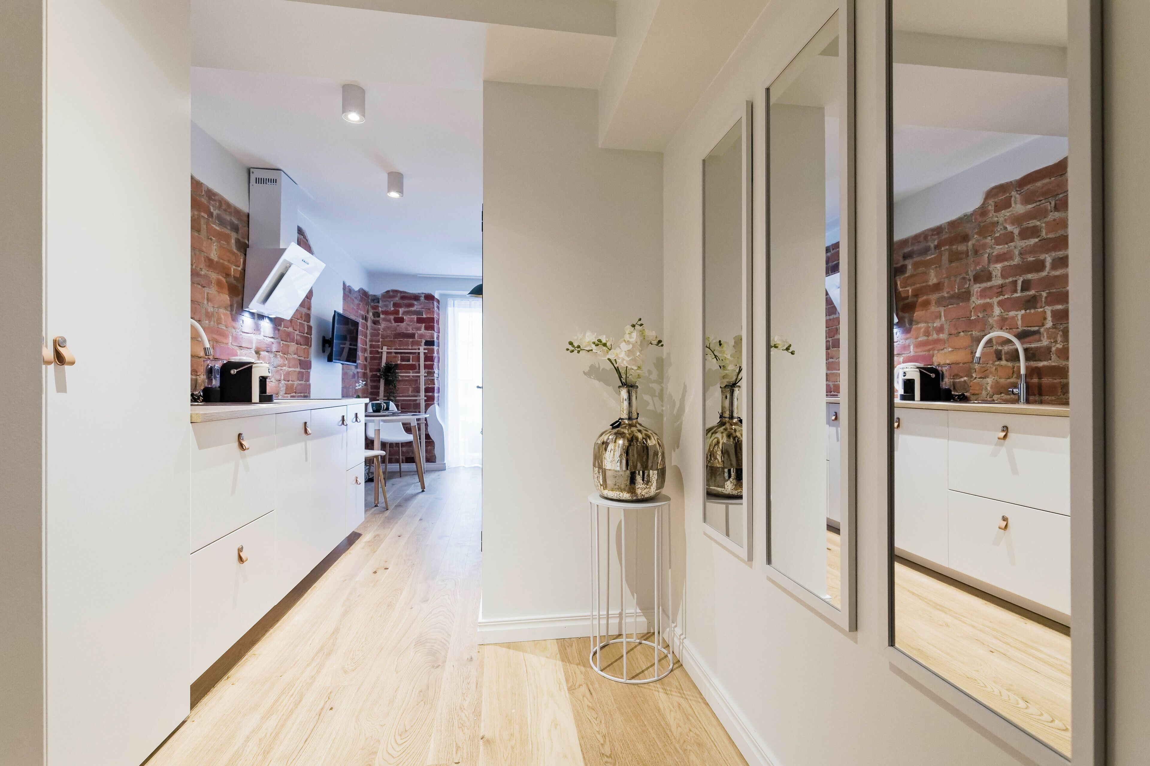 A modern kitchen with white cabinets, a brick wall, and a small round table with a vase.