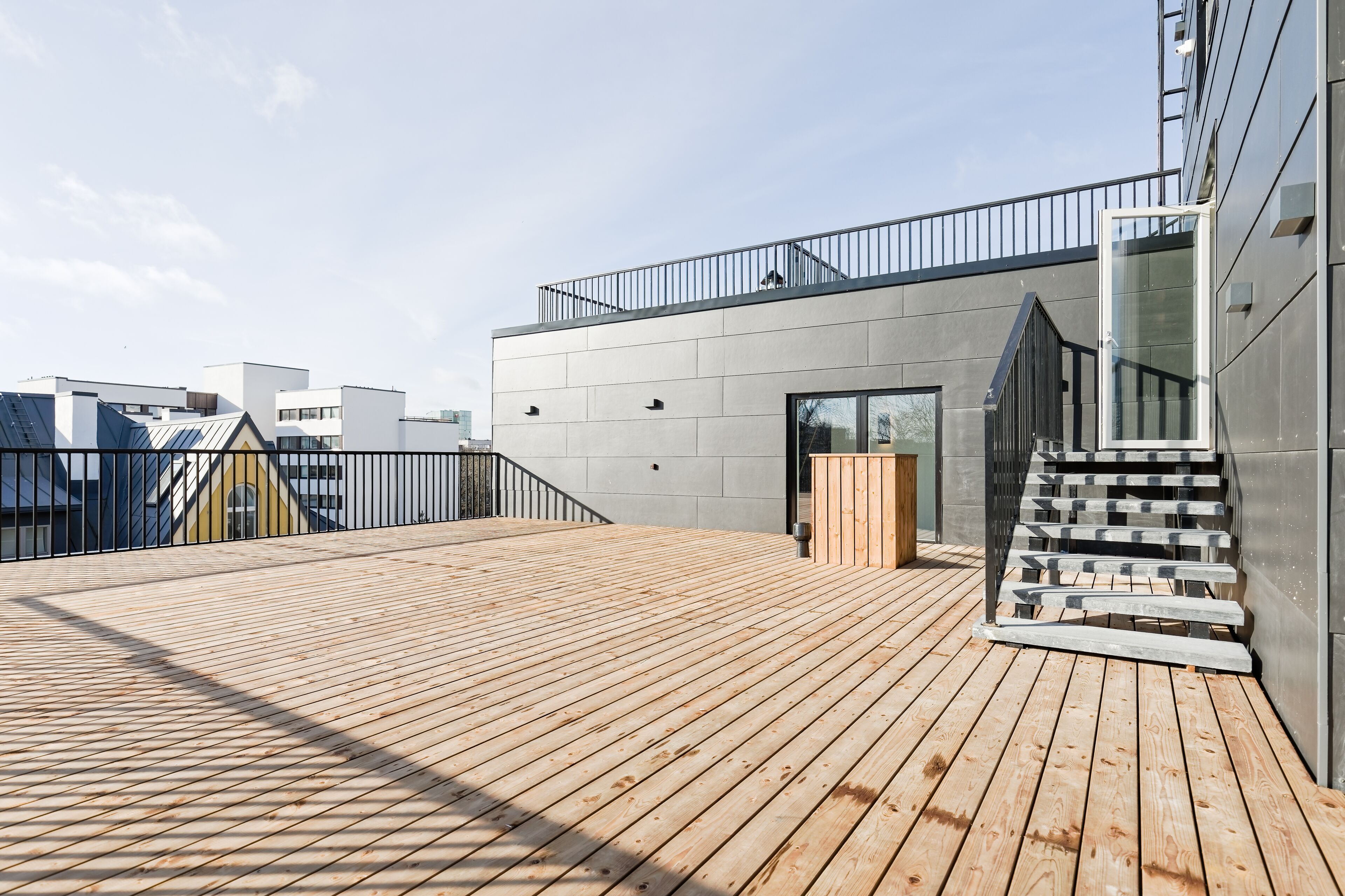 A modern building with a wooden deck, a staircase, and a glass door leading to an interior.
