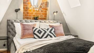 A bedroom with a tufted headboard, a brick wall, a large window, and two wall-mounted lamps.