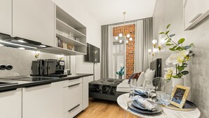 A modern kitchen with a built-in coffee machine, a dining area with a round table set for two, and a seating area with a view of a brick wall. - Bob W Tallinn City Centre - Avangard  (Tallinn)
