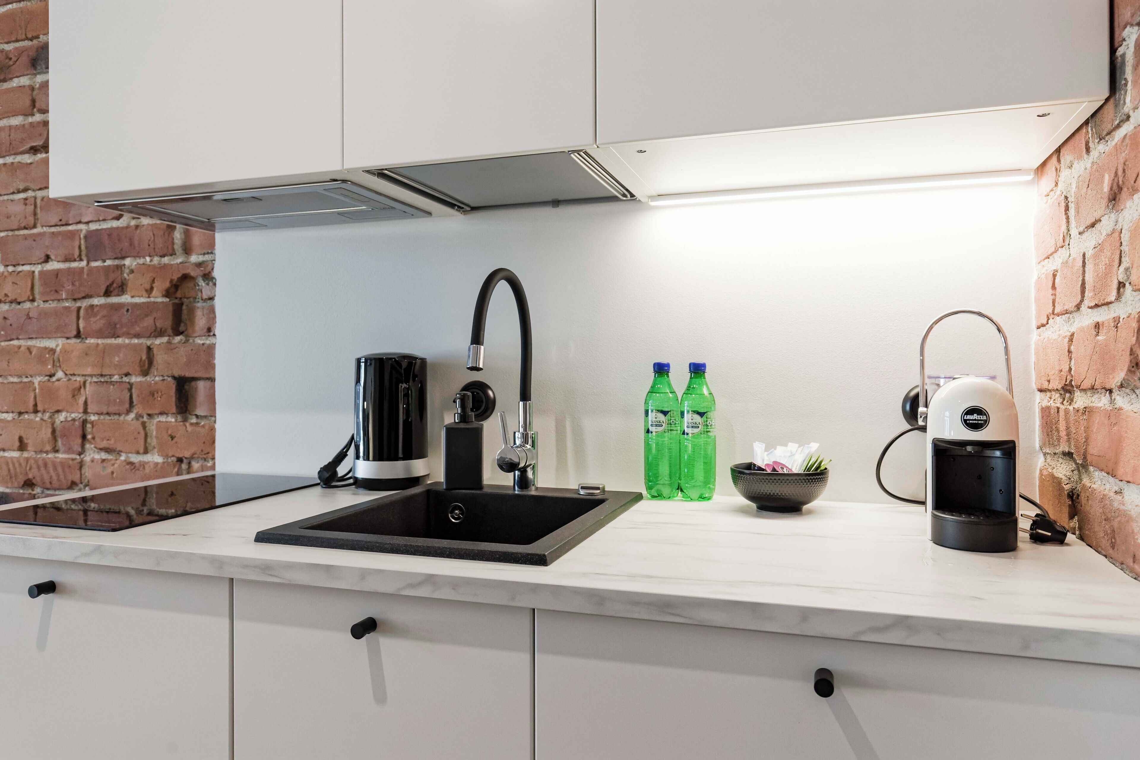 Een keuken met een zwarte spoelbak, een koffieapparaat en twee groene flessen op het aanrecht.