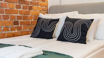 A hotel room with a brick wall, a bed with white bedding, two black pillows with white patterns, and a bedside lamp.