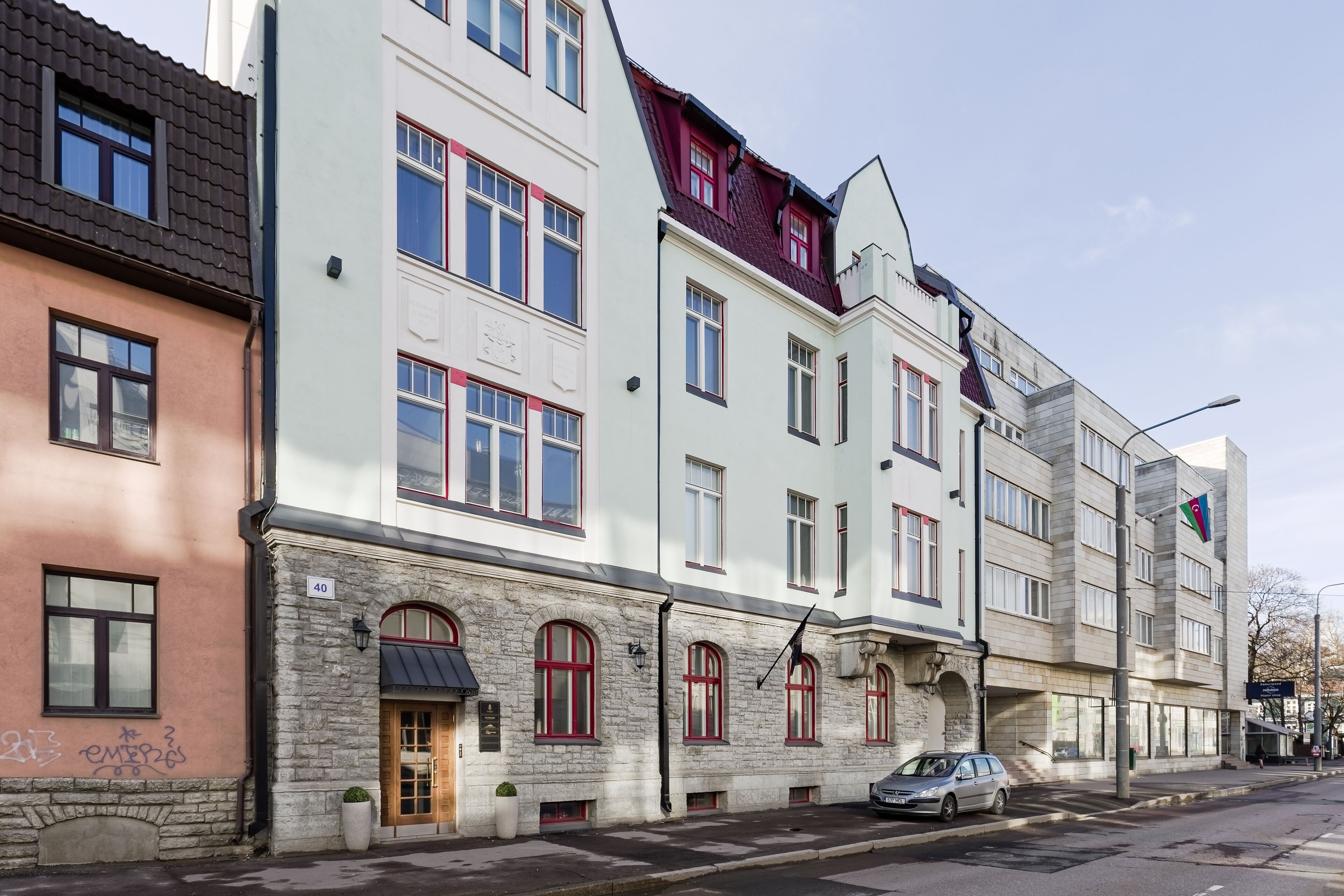 Eine Reihe mehrstöckiger Gebäude mit unterschiedlichen architektonischen Stilen, darunter eine Fassade aus Stein und ein modernes Design mit roten Fensterrahmen.