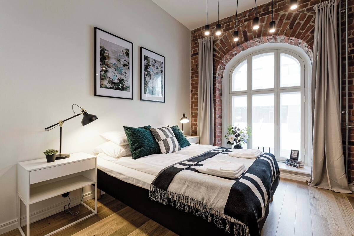 A modern bedroom with a large bed, a nightstand, a desk, and a window with curtains.
