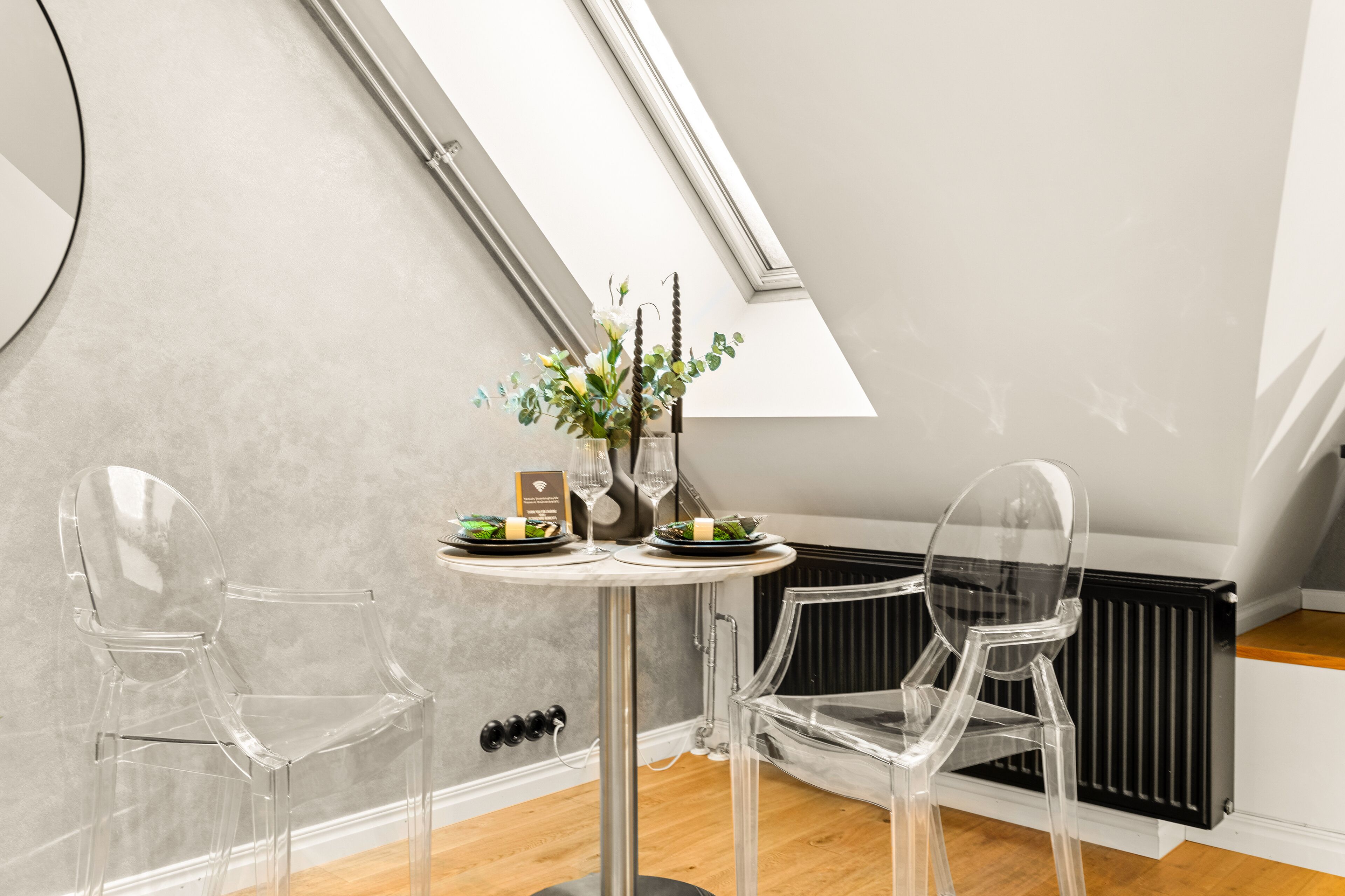 Ein modernes Zimmer mit Oberlichter, einem runden Tisch mit Blumenvase und zwei transparenten Stühlen.