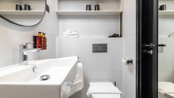 Un bagno moderno con un ampio lavandino bianco, un water e una zona doccia. Si notano mensole con articoli da toilette e una pianta.