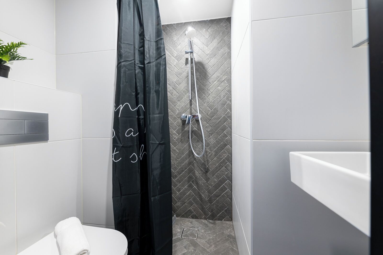 A modern bathroom with a shower, white tiles, and a black shower curtain.