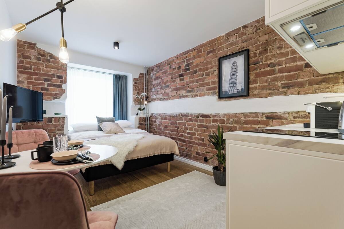 A modern bedroom with a brick wall, a bed, a desk, and a television.