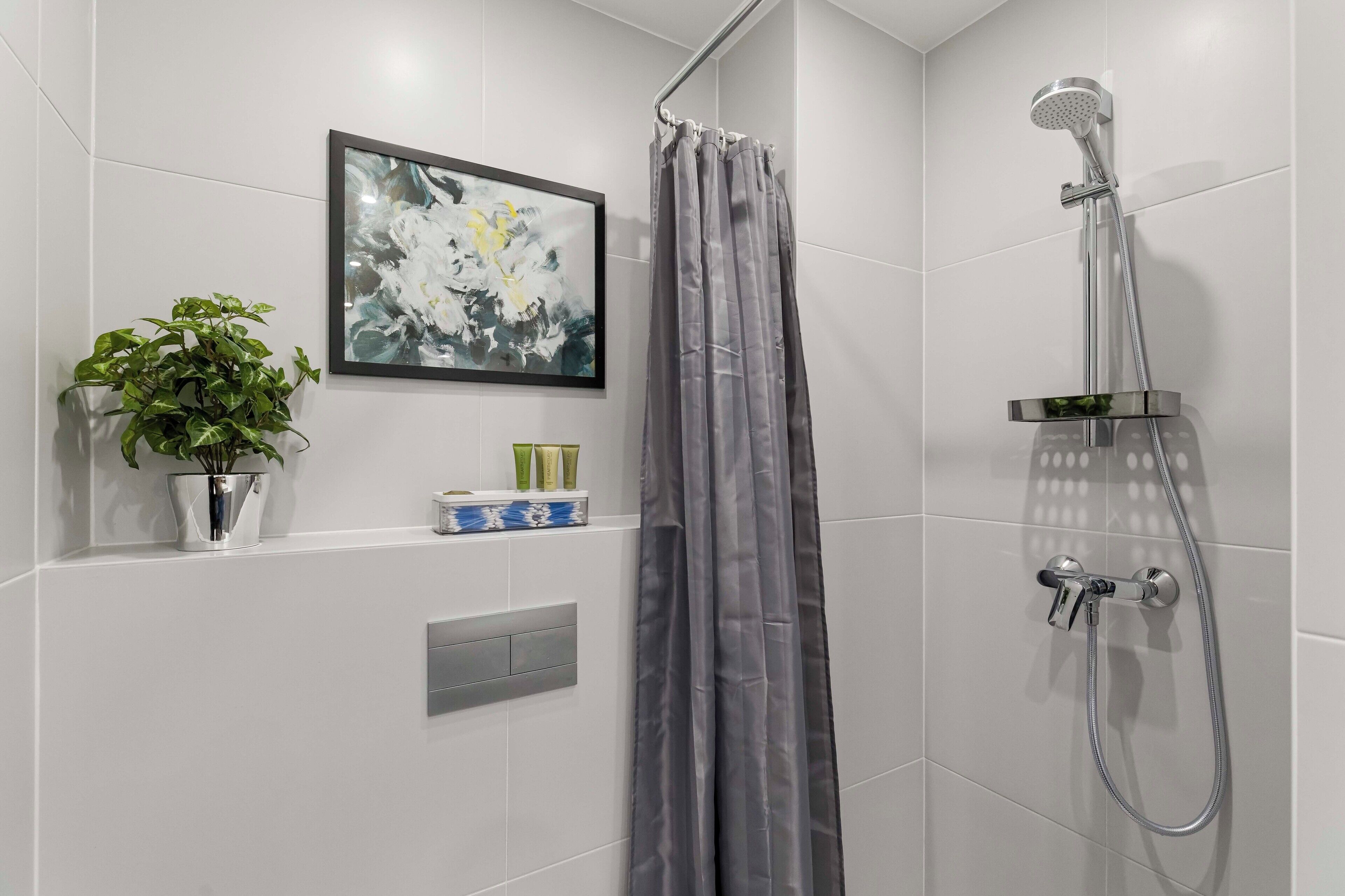 Un área de ducha moderna con una cortina de ducha gris, un cabezal de ducha montado en la pared y un estante con artículos de tocador.
