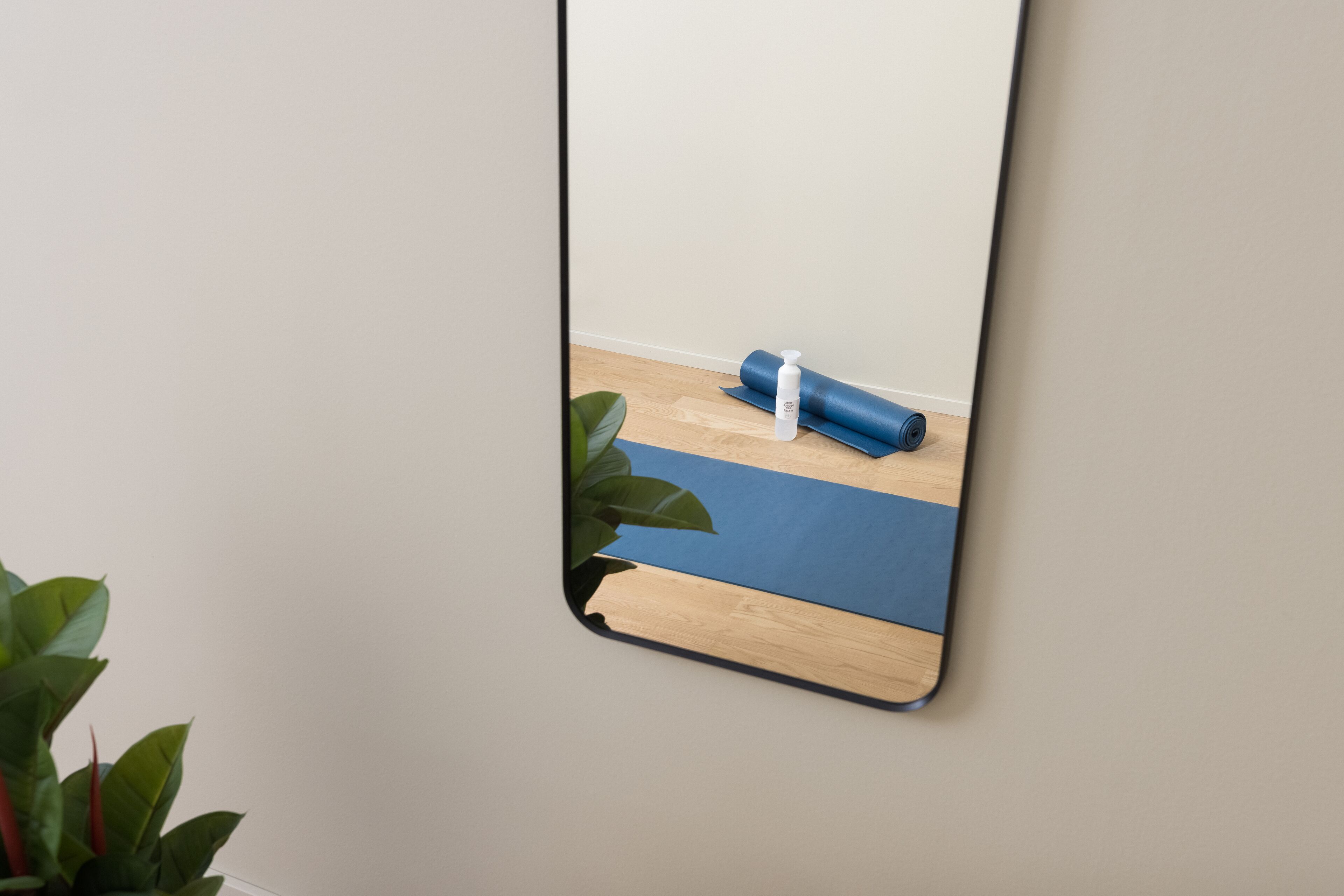 Een spiegel toont een yogamat, een yogoblik en een fles op een houten vloer.