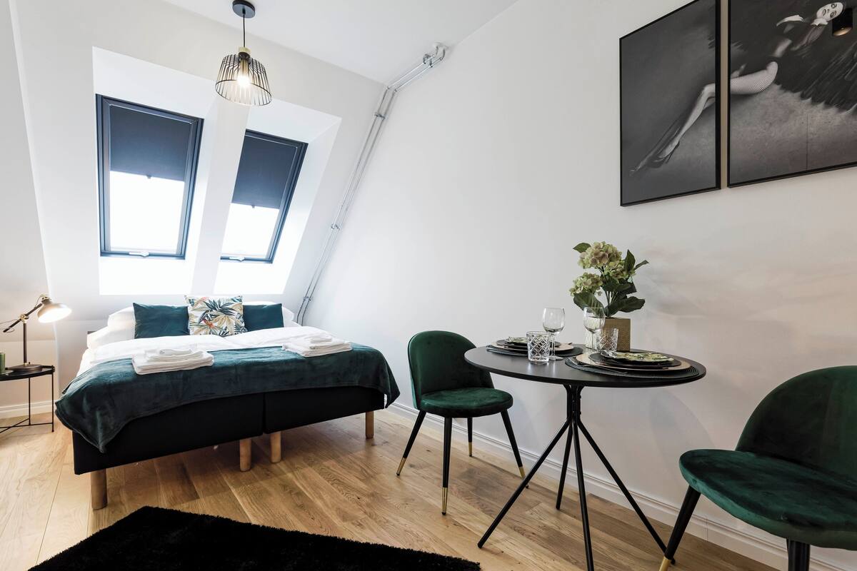 A modern bedroom with a bed, two chairs, a small table, and a window.