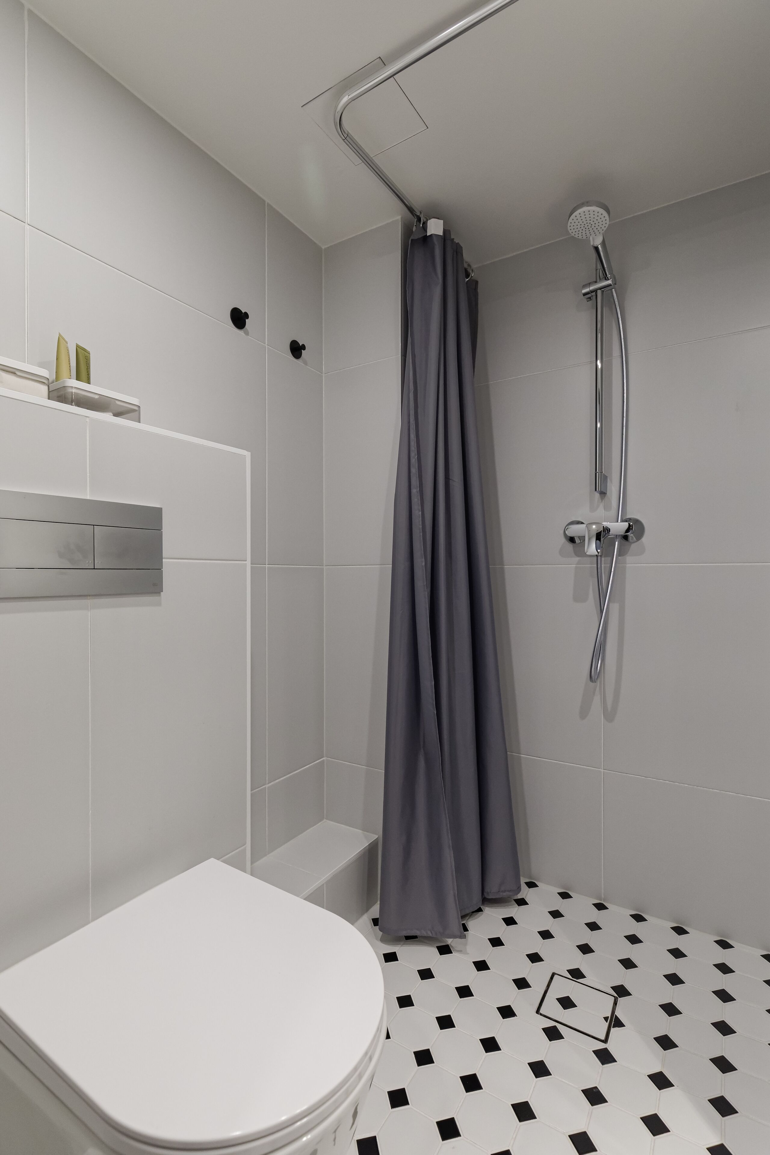 A modern bathroom with a white toilet, a shower with a grey curtain, and a tiled floor with a black and white pattern.