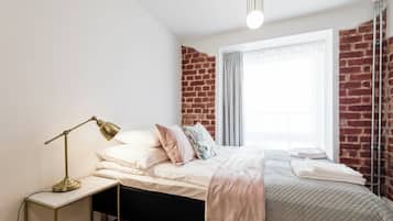 Ein Schlafzimmer mit Backsteinwand, einem Bett mit weißer Bettwäsche, einer Nachttischlampe und einem Fenster mit Vorhängen.