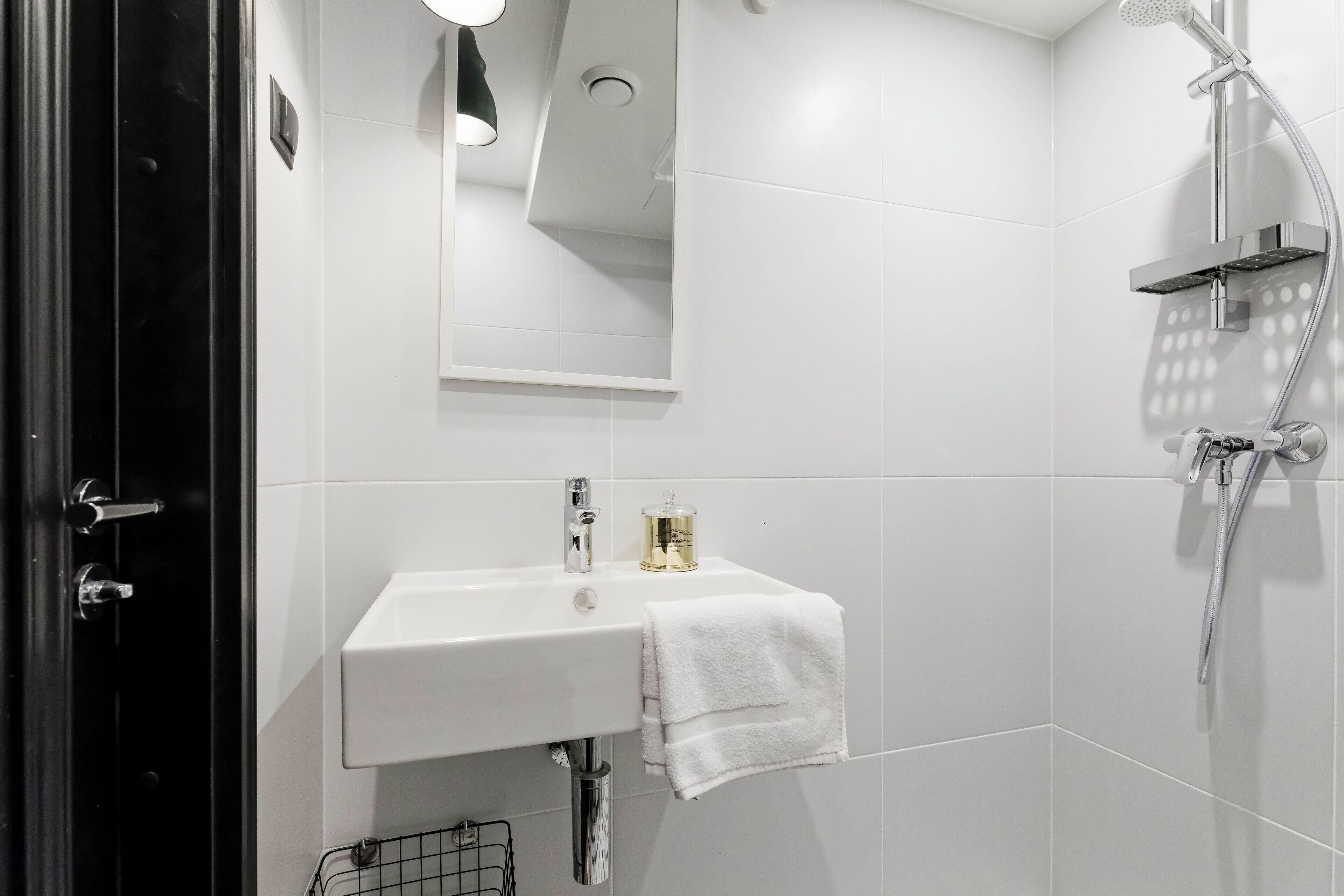A modern bathroom with a white sink, a mirror, a shower, and a towel hanging on the wall.