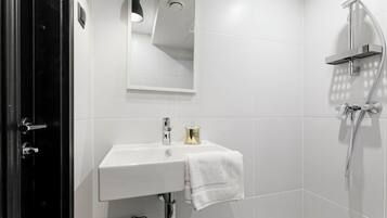 A modern bathroom with a white sink, a mirror, a shower, and a towel hanging on the wall.