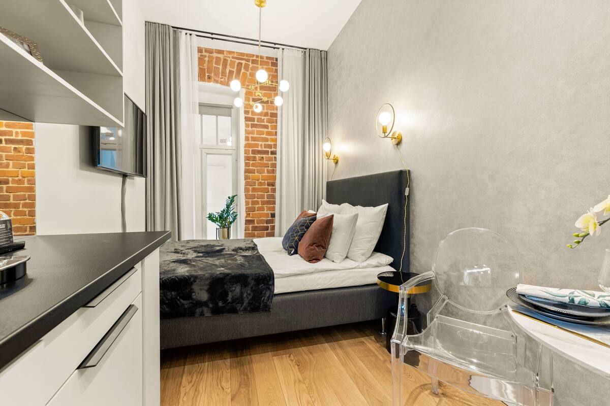 A modern bedroom with a bed, bedside table, and a clear plastic chair.