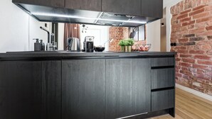 A modern kitchen with dark wood cabinets, a stainless steel range hood, and a brick wall. - Bob W Tallinn City Centre - Avangard  (Tallinn)