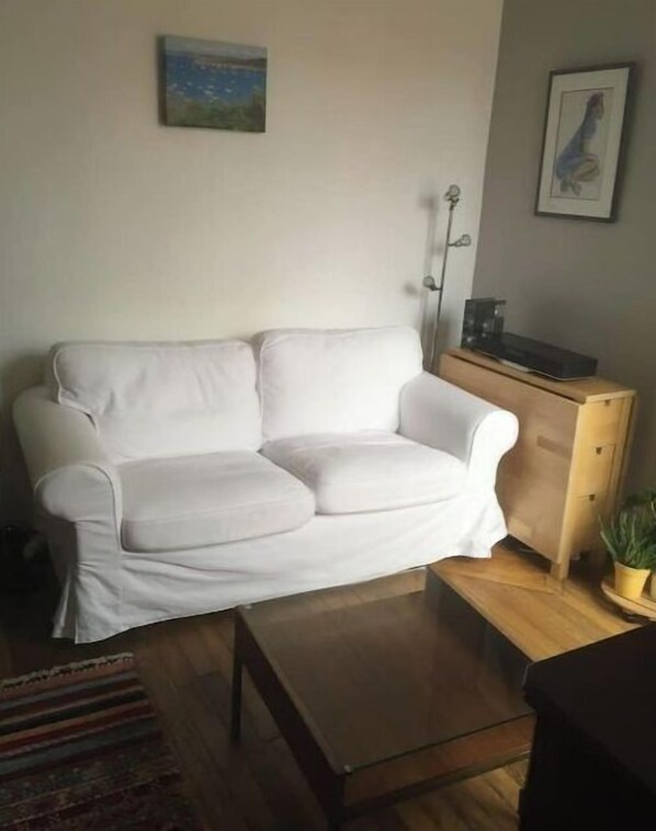 A white sofa in a living room with a wooden coffee table, a small plant, and a painting on the wall.