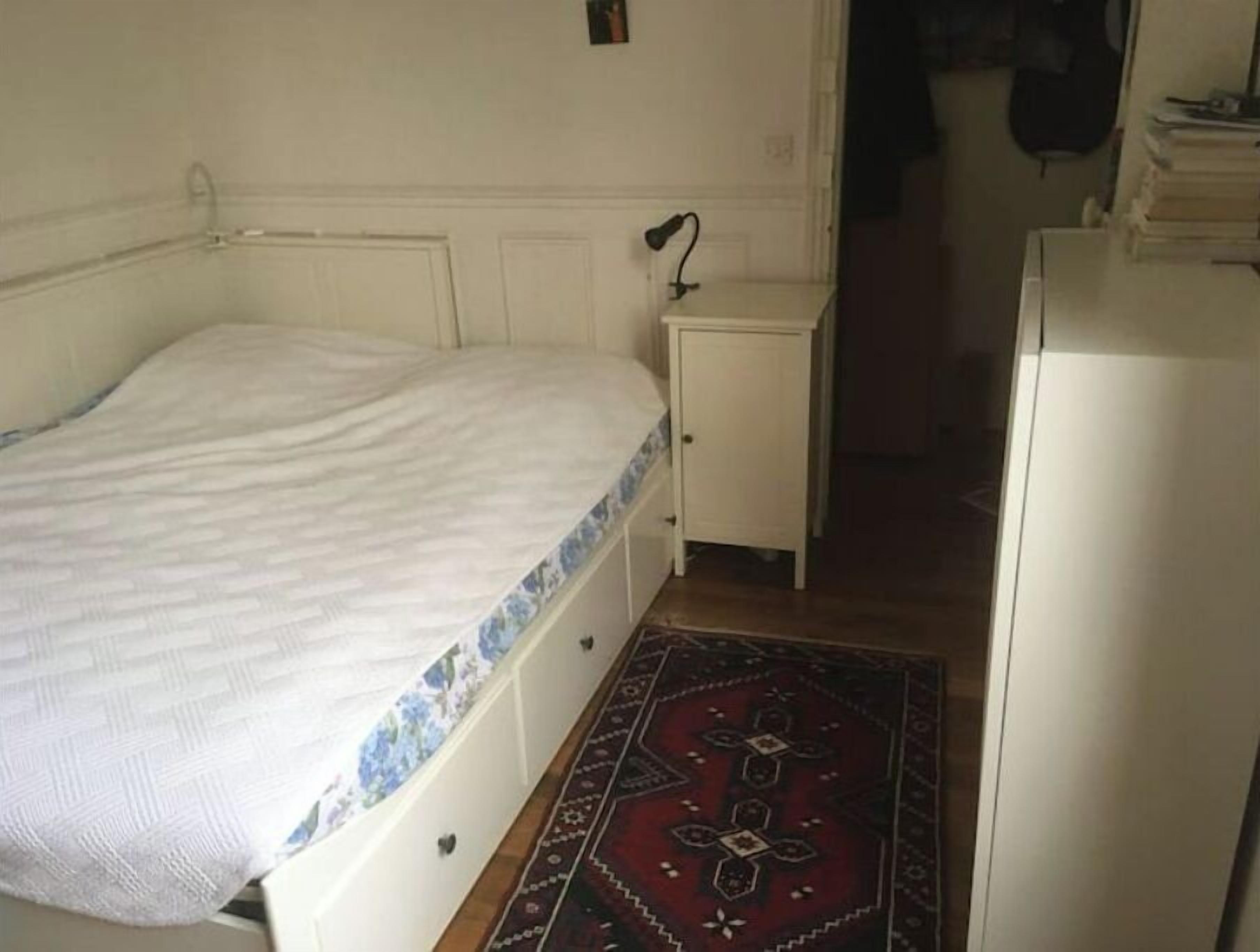 Ein kleines, schlichtes Schlafzimmer mit Bett, Nachttisch, Schreibtisch und einem gemusterten Teppich.